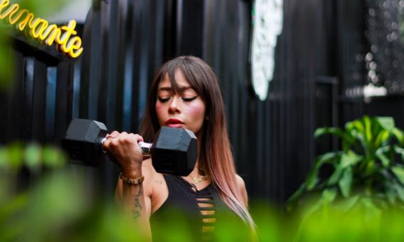 Fitness woman with long hair lifting a dumbbell outdoors, focusing on her strength training.